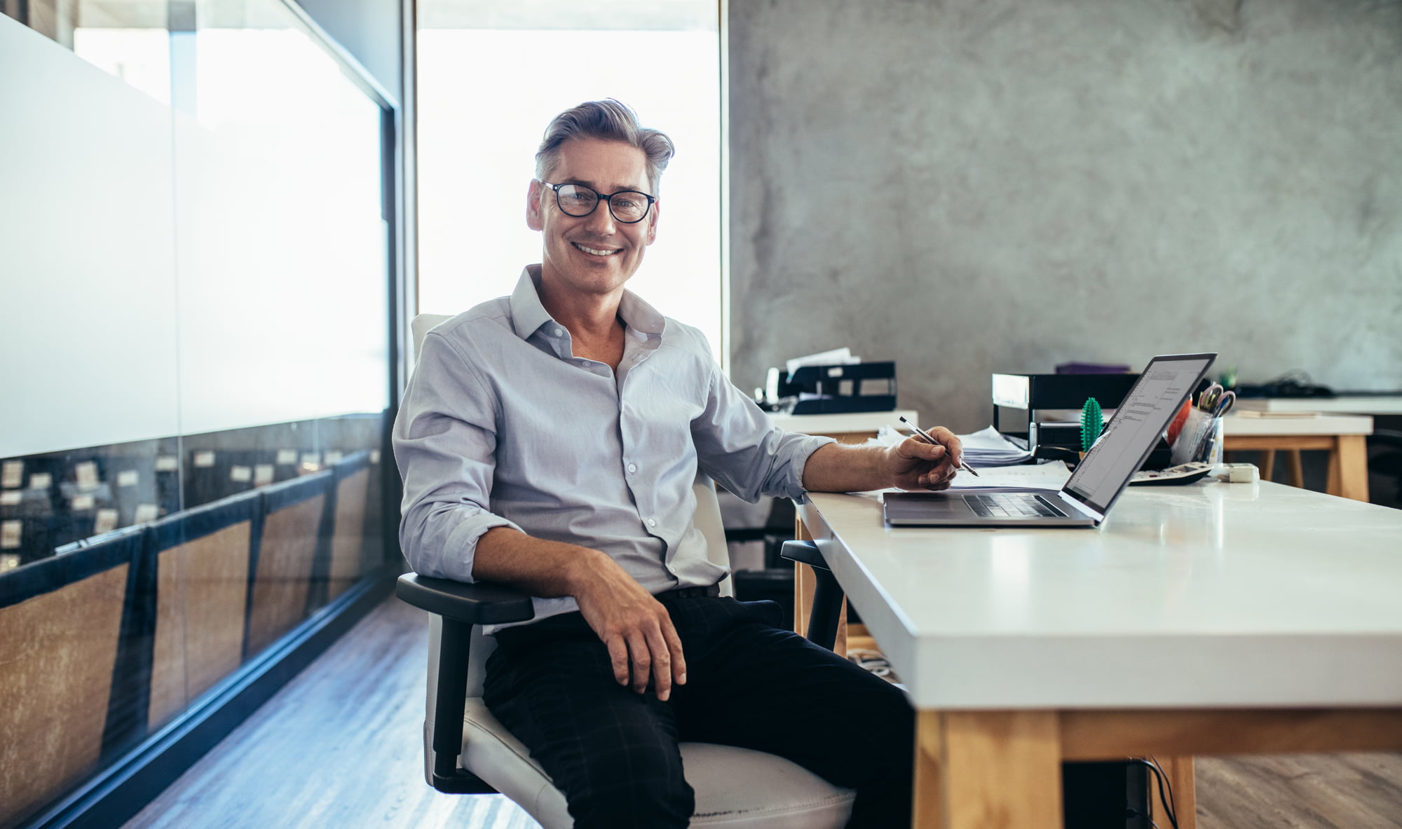 Hôtelier souriant travaillant sur un ordinateur portable dans un bureau moderne, illustrant la gestion du pré check-in et du self check-in pour améliorer l’autonomie des clients.
