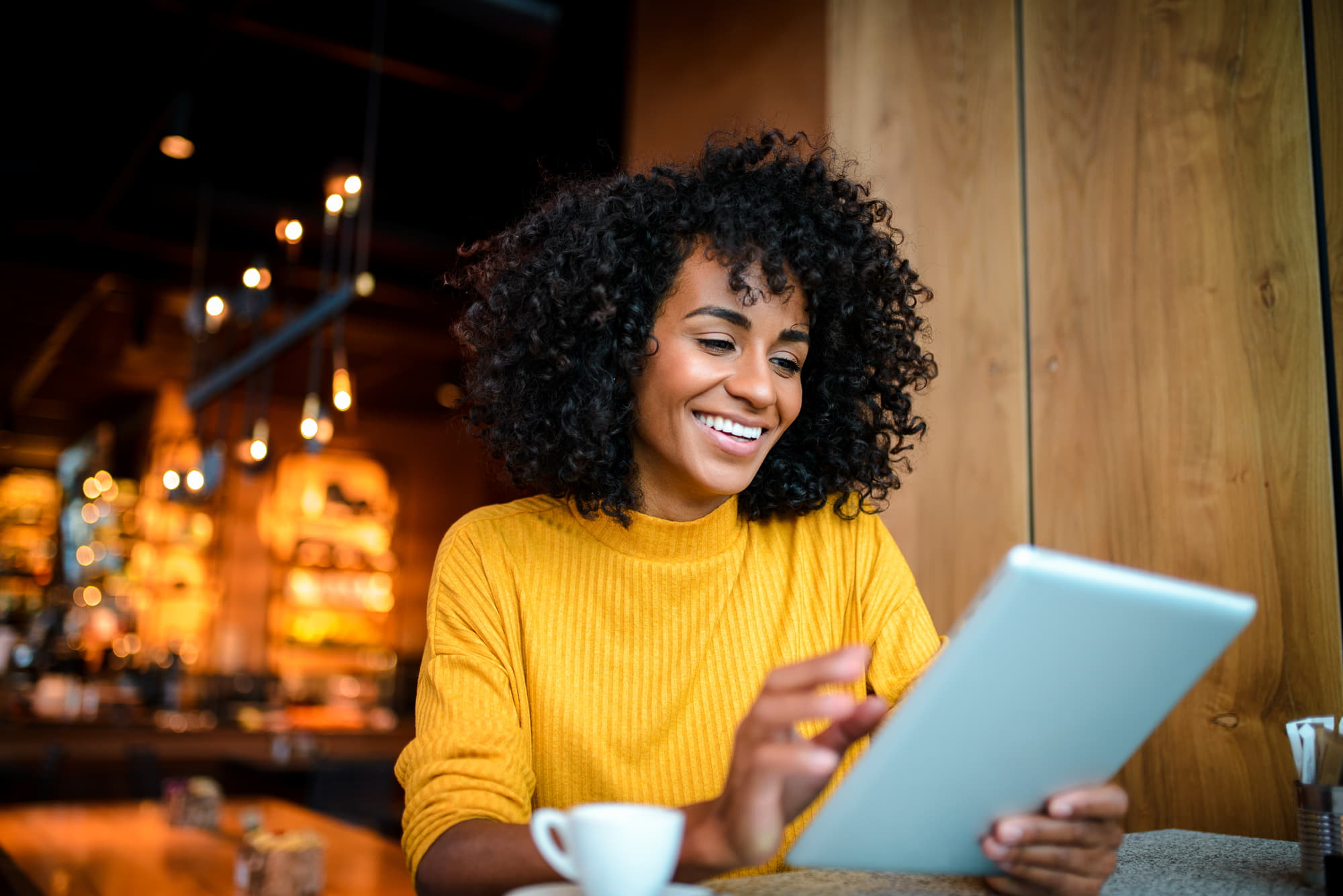 Cliente utilisant une tablette dans un café, illustrant les solutions digitales permettant aux hôteliers de gagner du temps et d’optimiser la gestion en 2023.