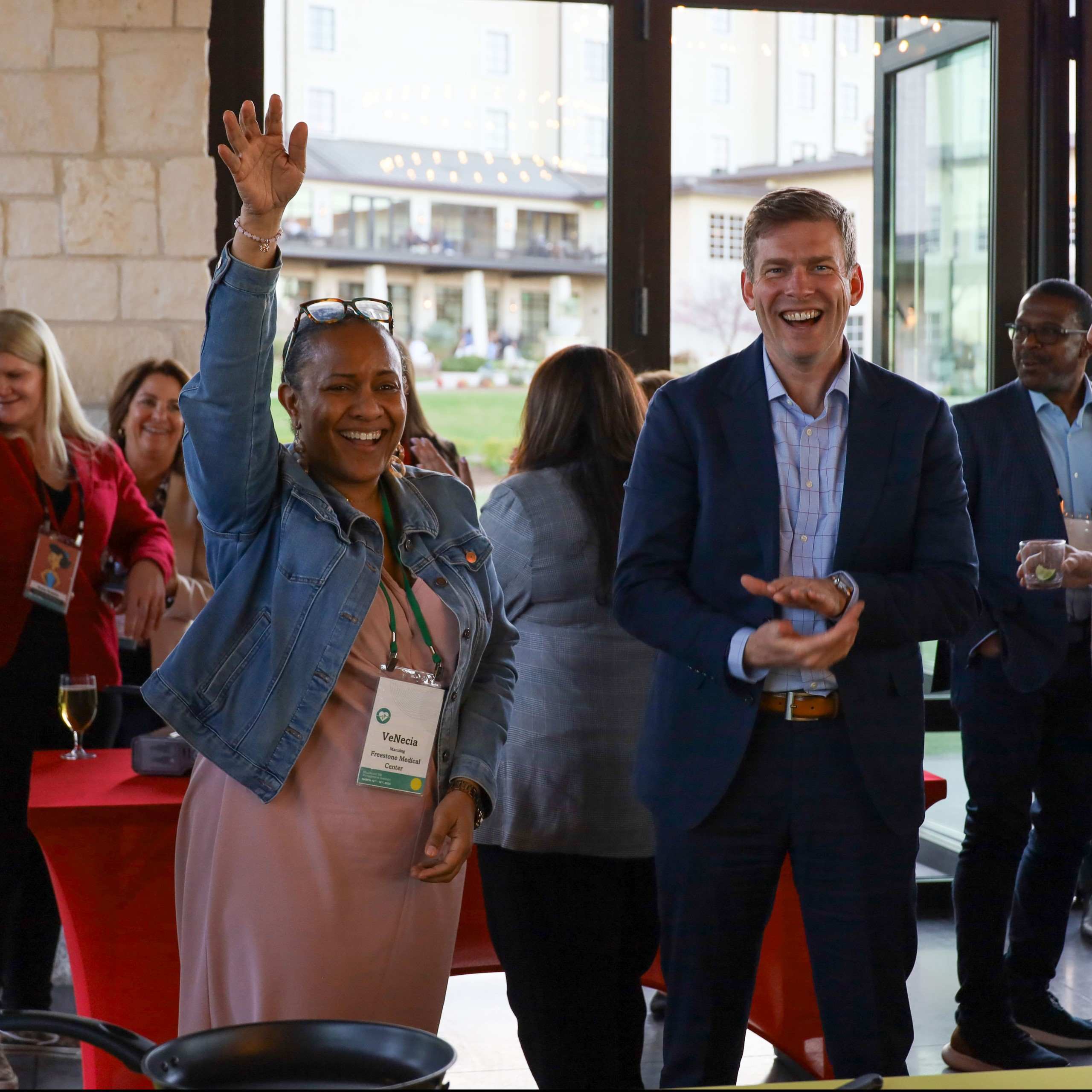 Attendees smiling and raising a hand at an IPMI networking reception