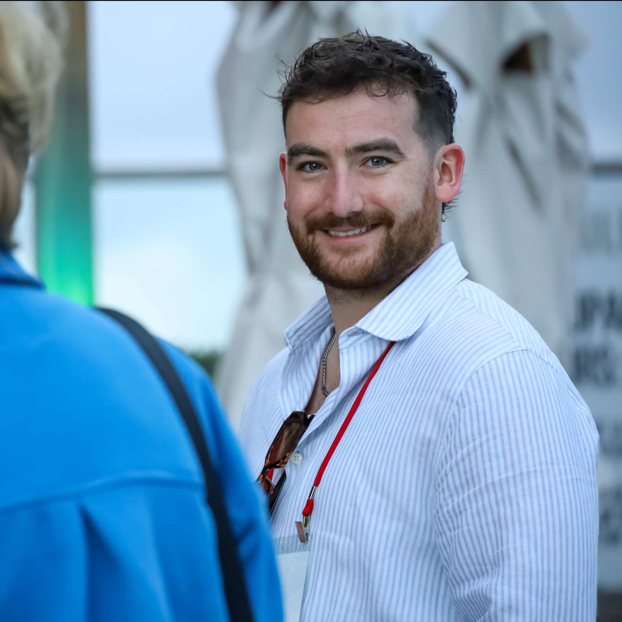 A smiling participant wearing a striped shirt and event lanyard at an IPMI gathering