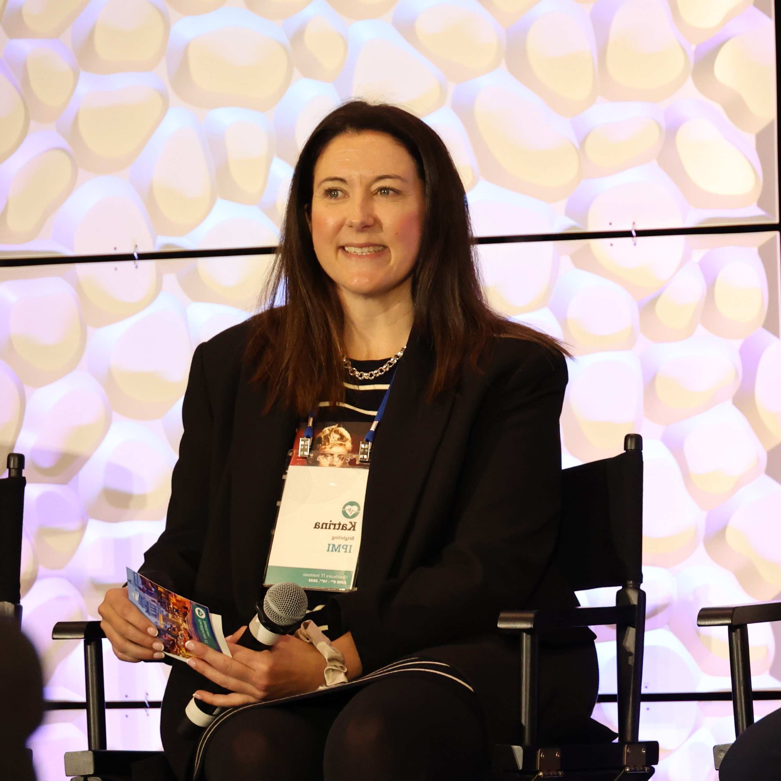 Seated panelist holding a microphone and notes during an IPMI session