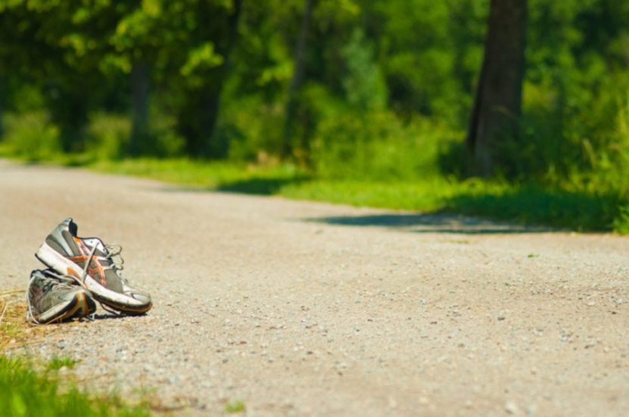 An image of a track with a couple of sneakers laying down. A tree and grass in the background.