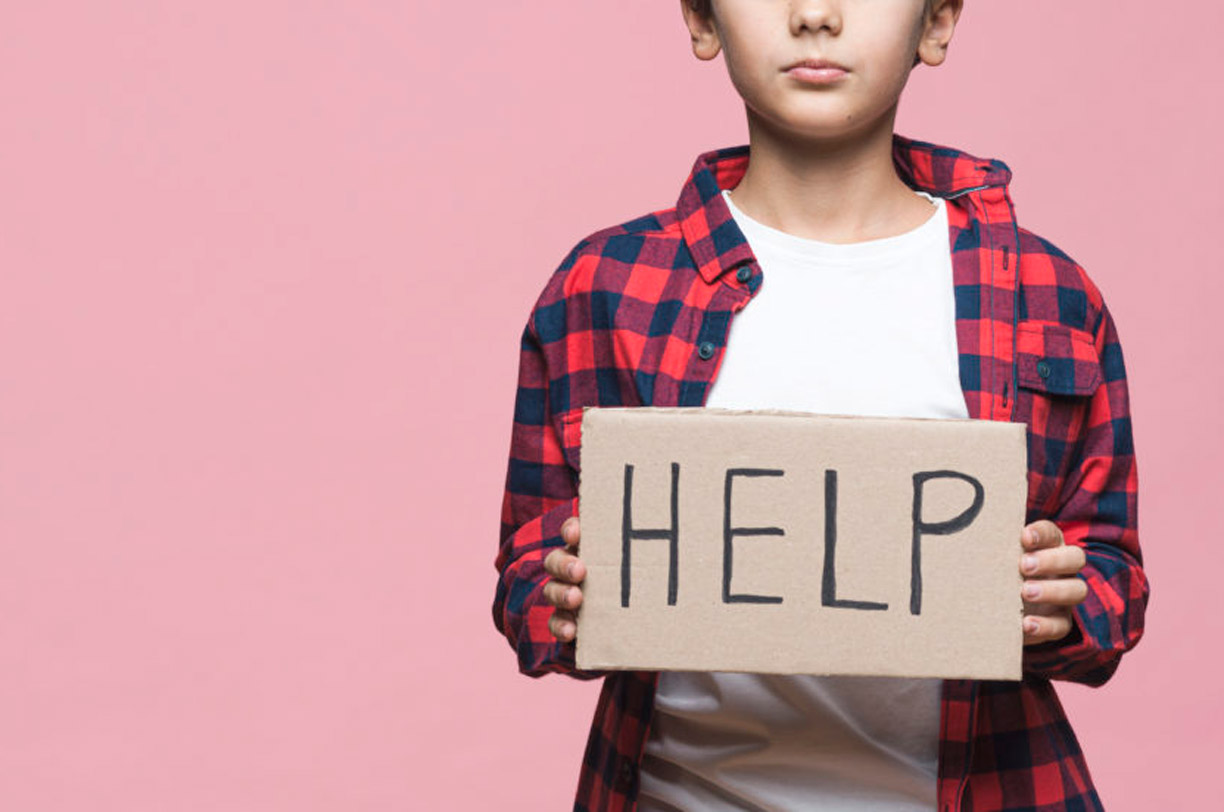 An image of a boy holding a carton sign that says help/