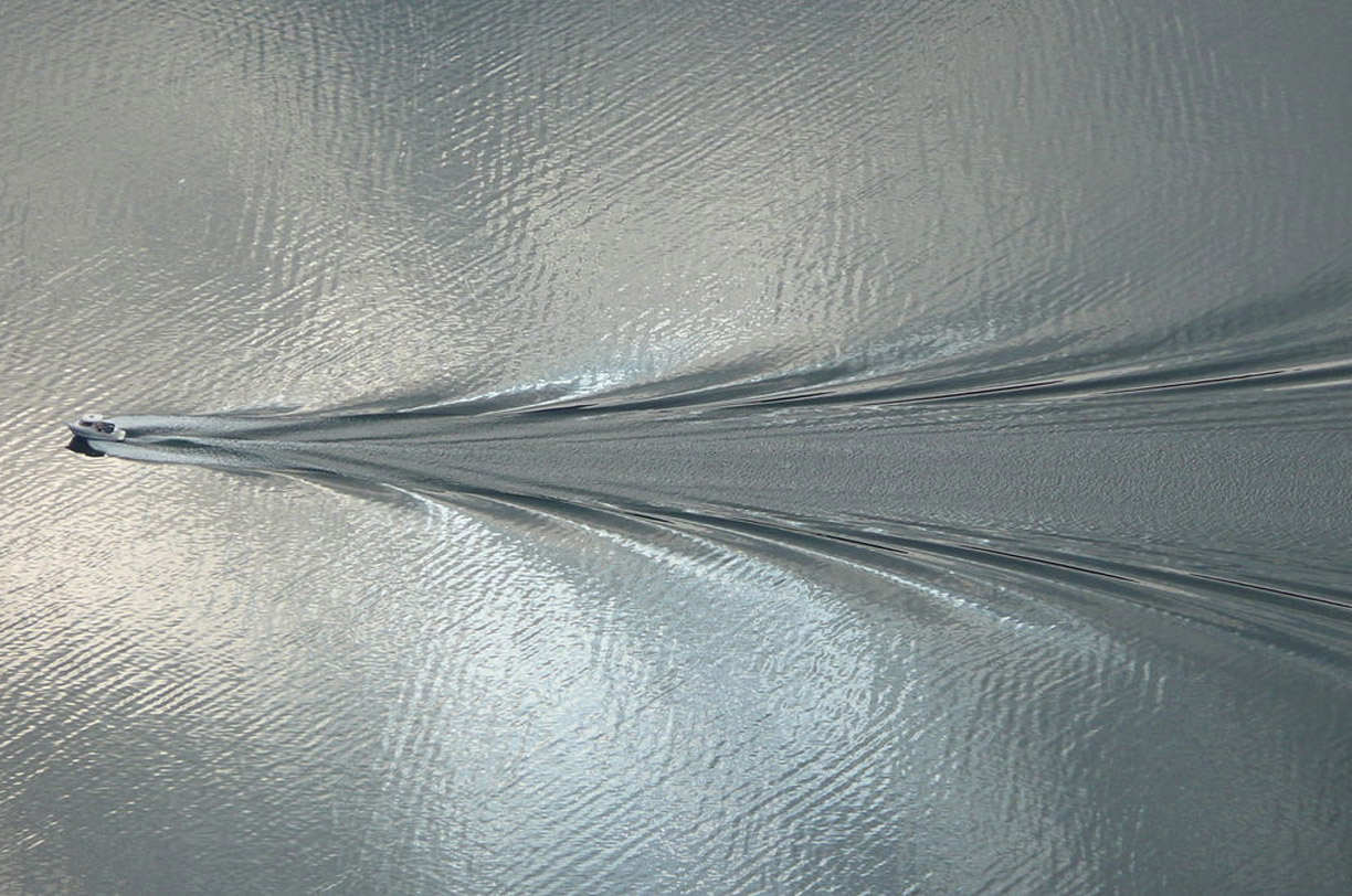 An aerial image of a boat sailing and leaving a water trail.