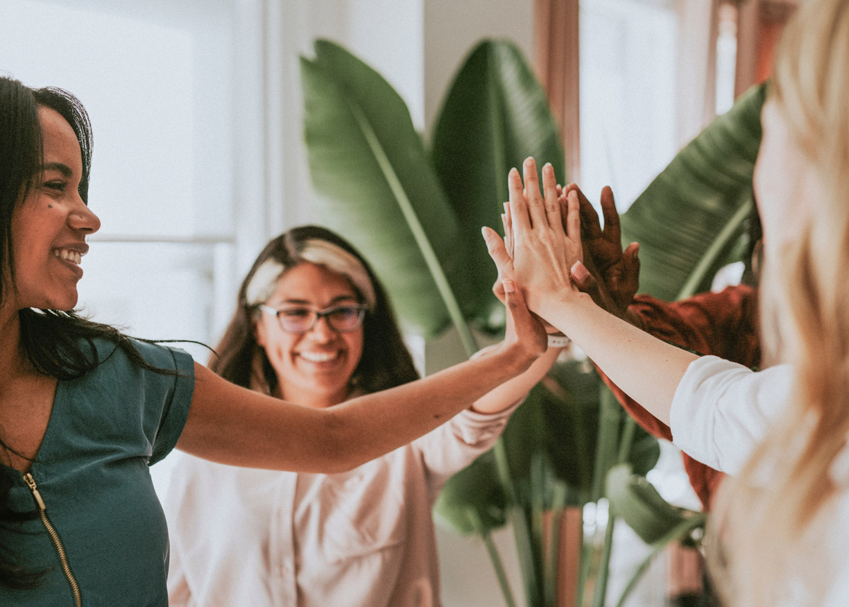 Team of diverse women putting their hands together to show how they work together to shape a better future.