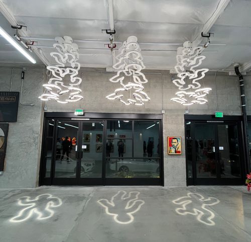 Three human shaped chalk outline chandeliers hang in a concrete gallery.