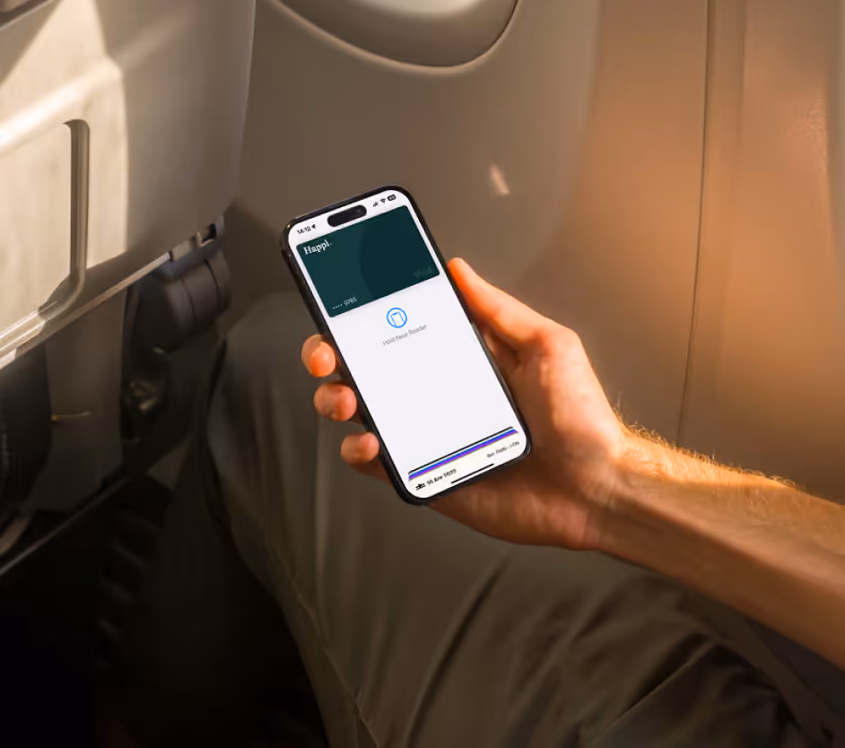 Hand holding a smartphone inside an airplane, showing a contactless payment screen with a digital card labeled 'Happl.'
