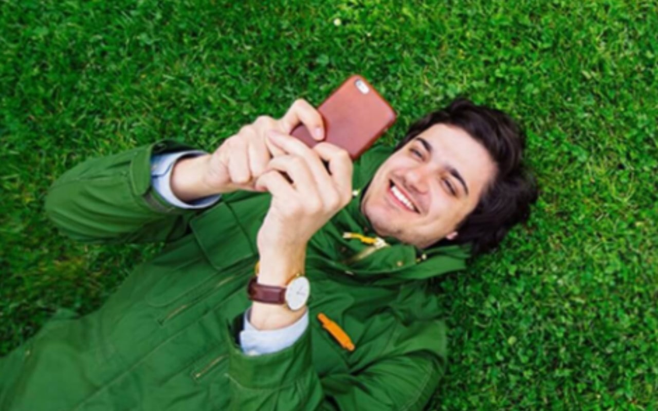 Man with his phone laying in grass.