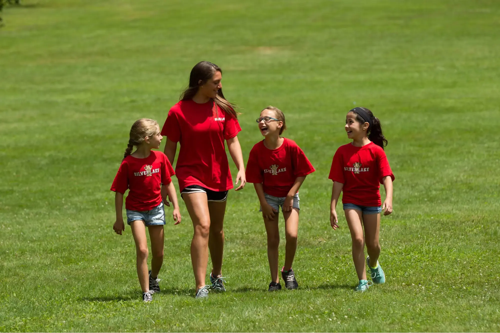 A camp counsellor and three campers walking on a grass field at Camp Silver Lake