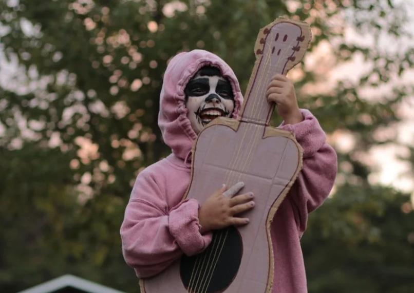 Camp Anne camper with face paint and a cardboard guitar prop for a performance