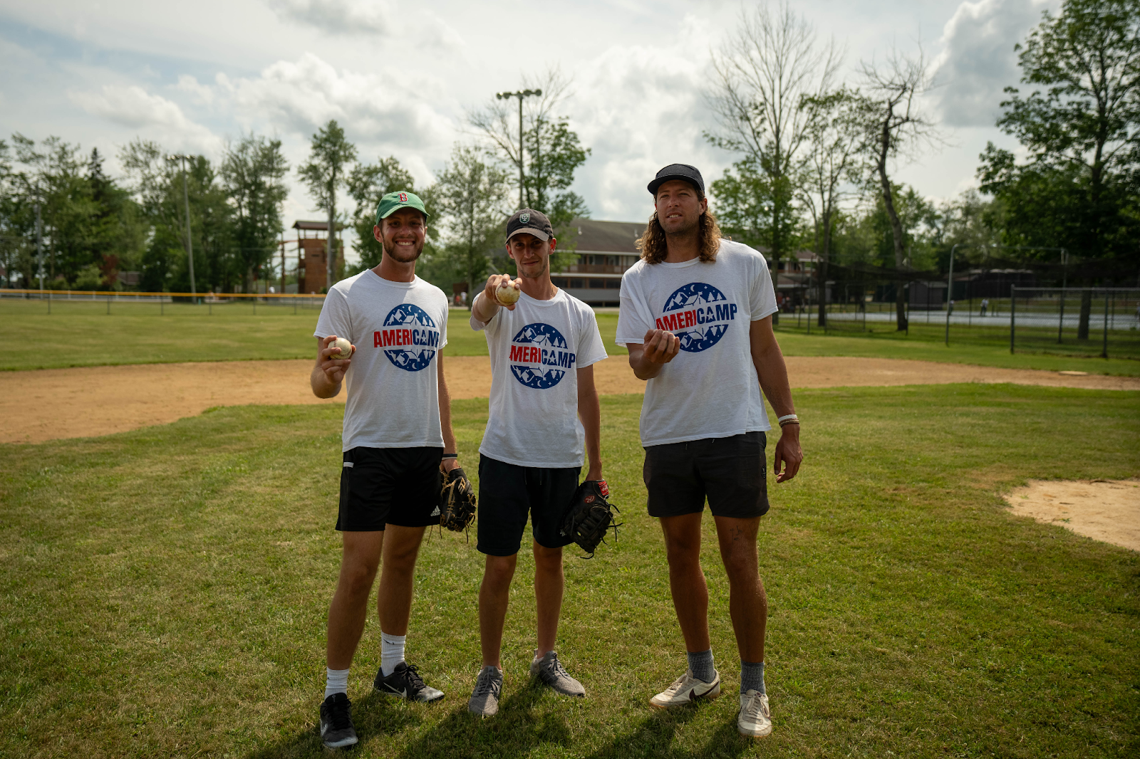 Three AmeriCamp counsellors with baseball mitts and balls on a diamond