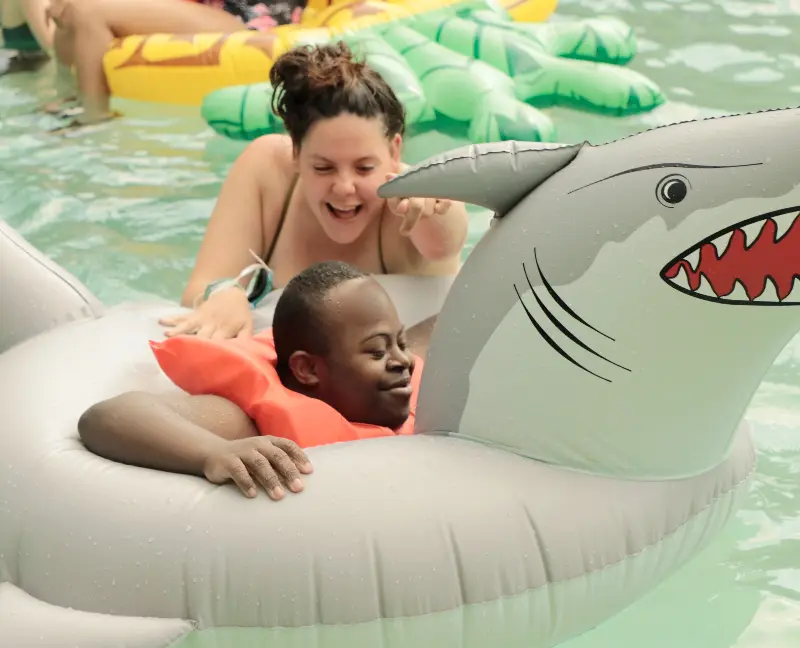Camp counsellor and camper at Camp Anne playing on an inflatable pool toy