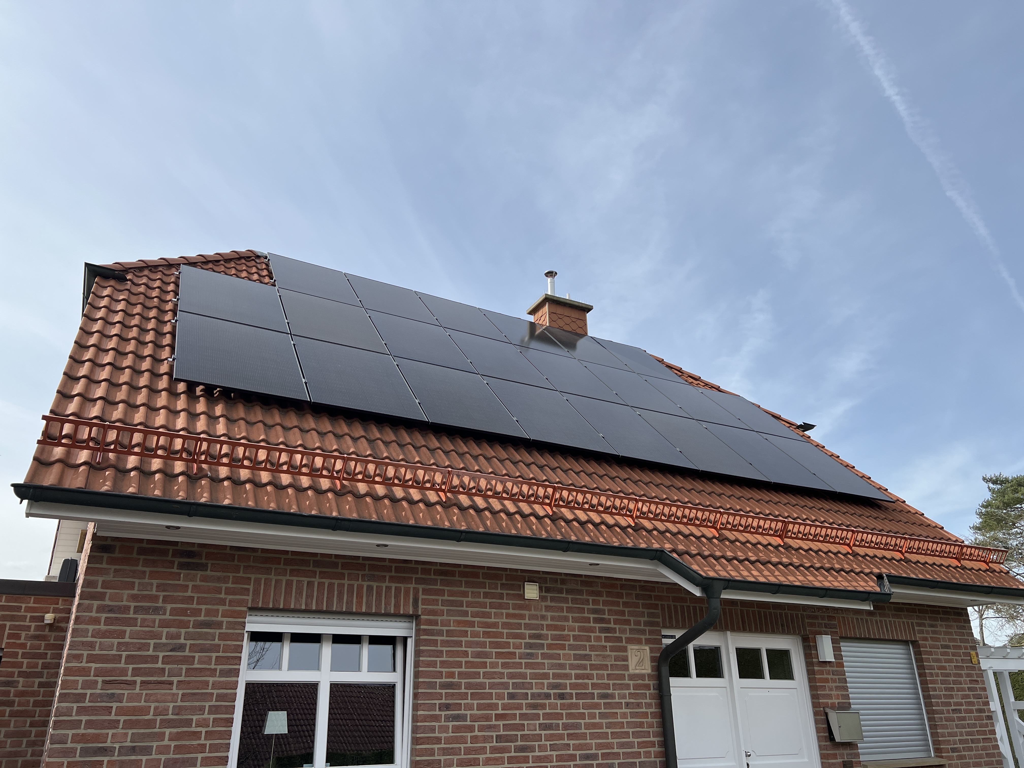 House with brown tiled roof featuring black solar panels installed under a blue sky.
