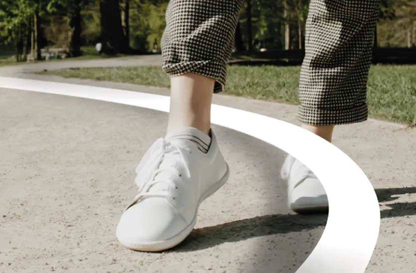Person wearing checkered pants and white sneakers walking on a curved paved path outdoors.