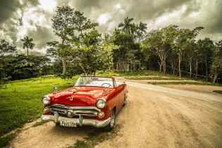 old red convertible on a dirt road with trees in the background
