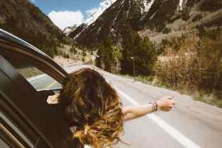 rear view of a lady hanging out the passenger window enjoy the breeze on a road lined with mountains