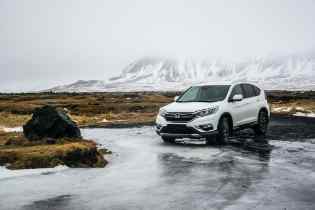 white car a a wet road with snow capped mountains in the background