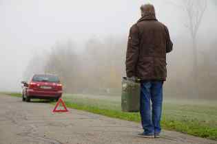 rear view of a man walking towards his broken down car with a gas canister in the fog