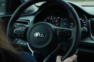 close up of a kia steering wheel with the driver's hand on the bottom part