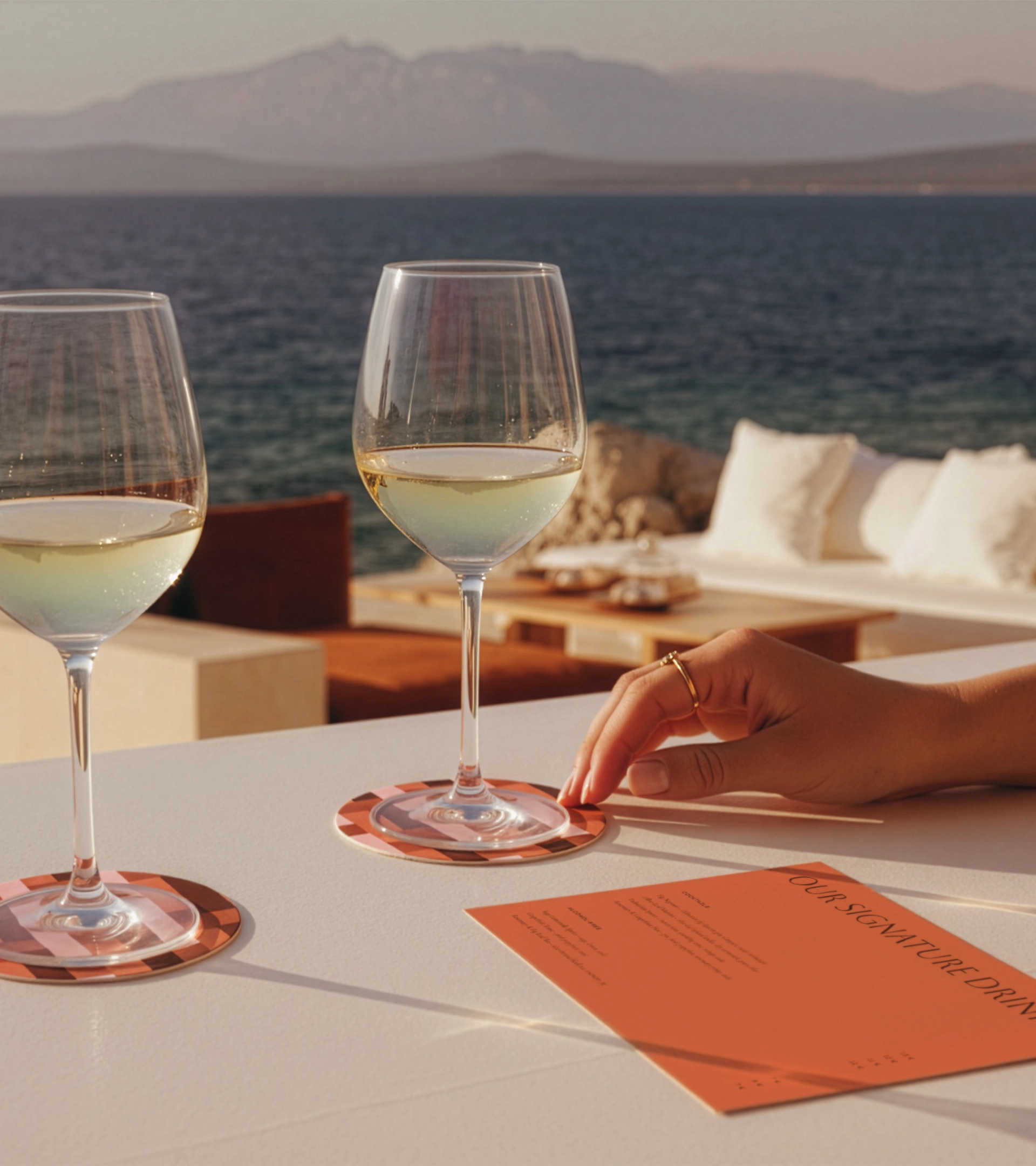 Table dressée en plein air avec verres à vin blanc, plateau de fromages et serviettes griffées Villa Luka avec le logo du taureau ailé, vue sur la mer Adriatique et les montagnes lointaines