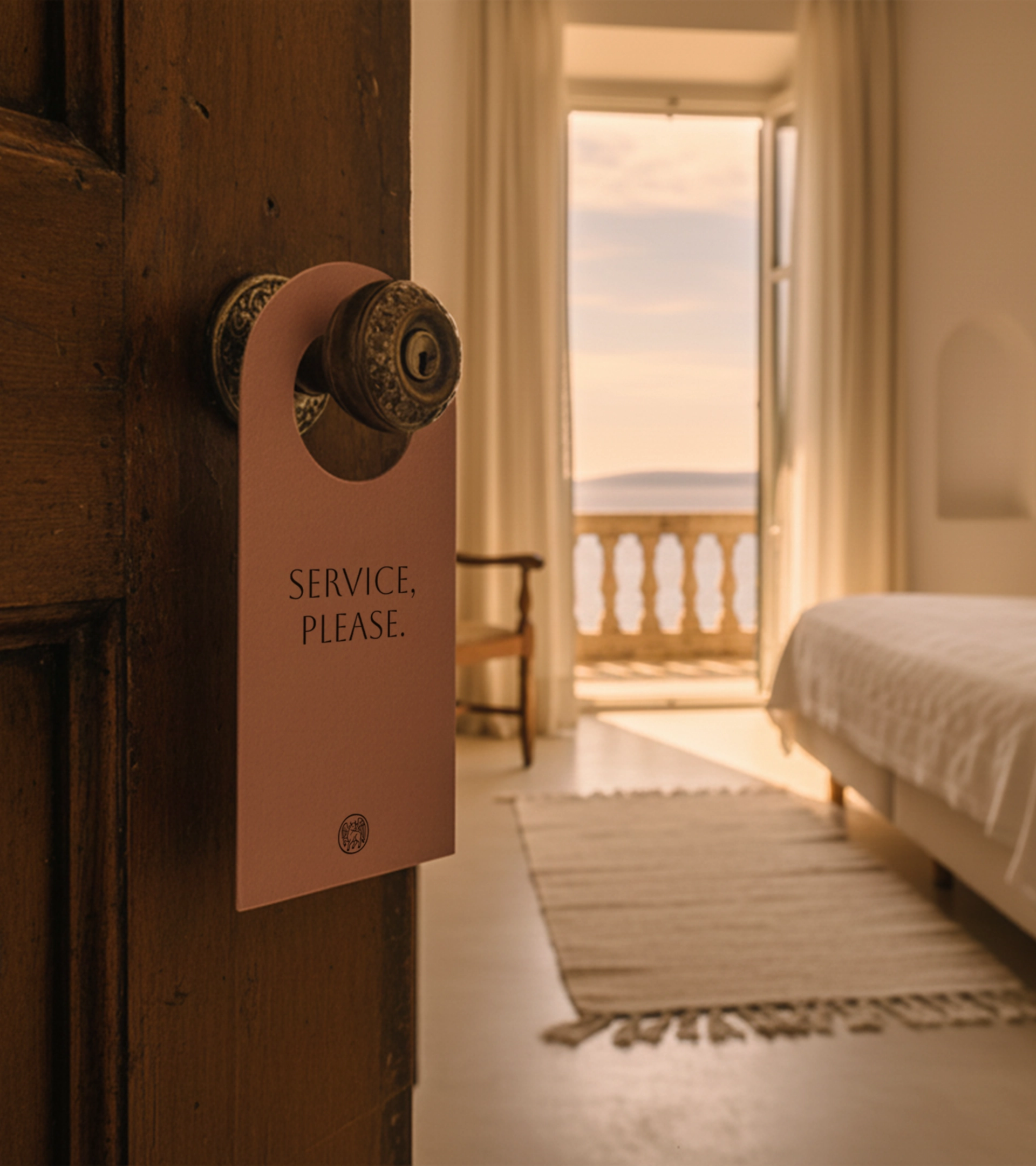 Poignée de porte d'hôtel avec accroche-porte « Service, please », montrant l'intérieur chaleureux d'une chambre méditerranéenne avec vue sur la mer