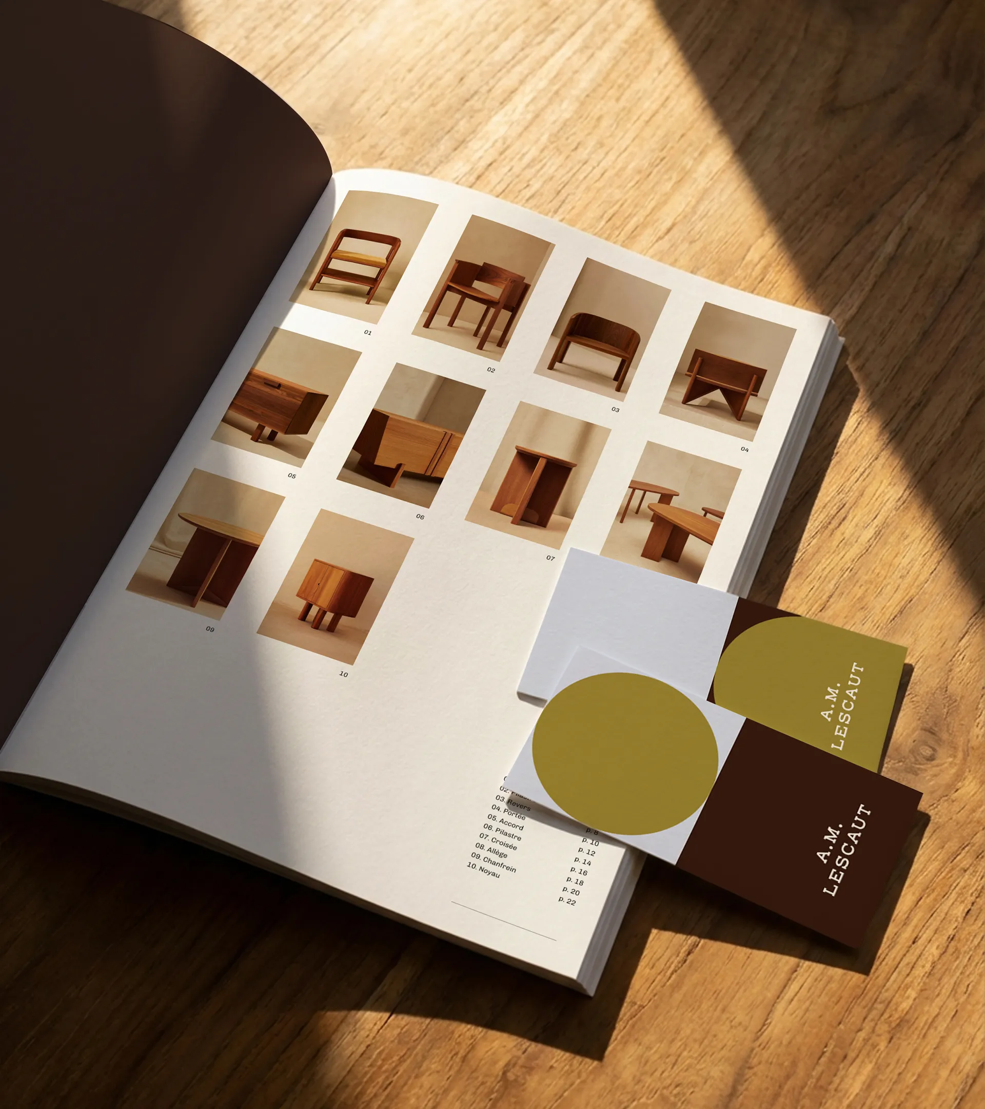 Catalogue ouvert posé sur un sol en bois, présentant des images de meubles en bois, avec deux cartes de visite portant la mention « A.M. Lescaut » posées dessus.