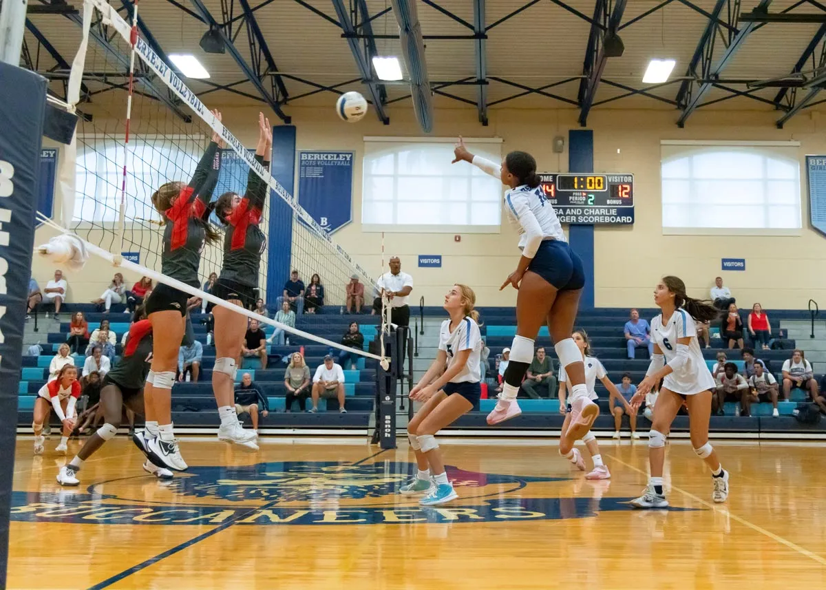 Varsity girls' volleyball team; player goes up to spike the ball