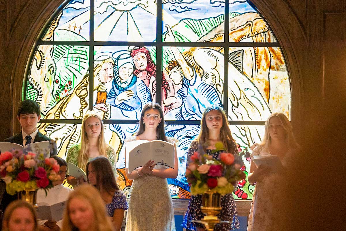 Student singers standing in front of a stained glass window during the consecration of the Berkeley Chapel