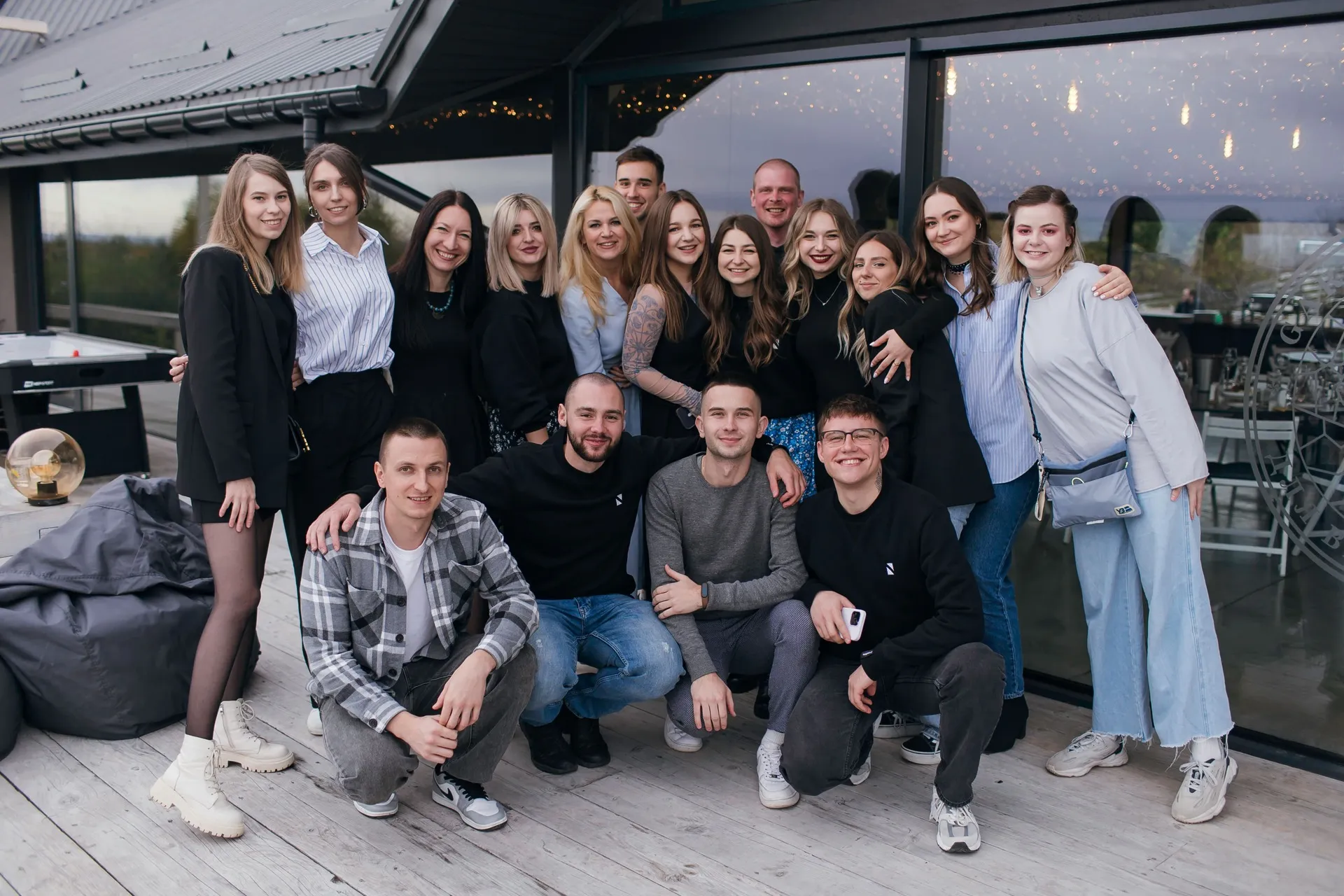 Group of smiling young adults posing closely outside a modern building with glass walls.