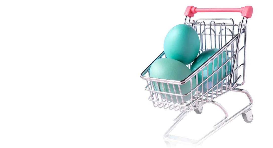 Mini shopping cart with four blue and teal eggs inside on a white background.