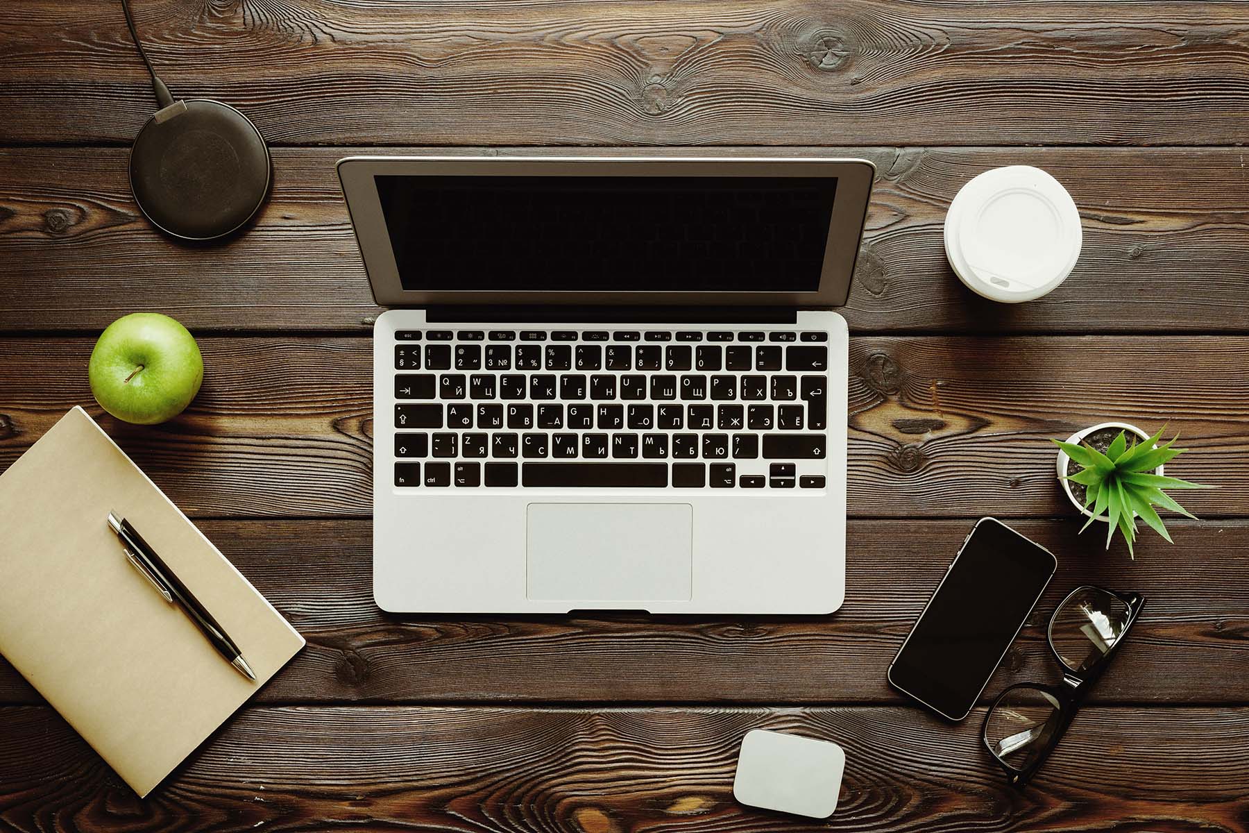 aerial view of desk with laptop, coffee, plant, cellphone, notebook, charger, apple, glasses and cell phone