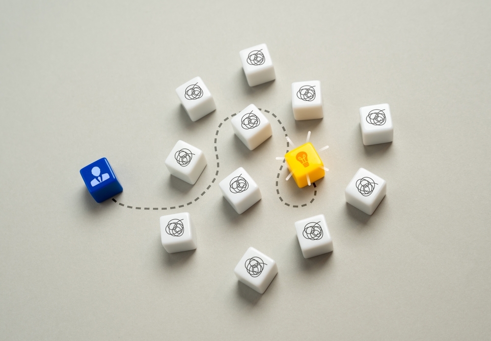 A blue figure navigates a path through white cubes representing problems to reach a glowing yellow idea cube.