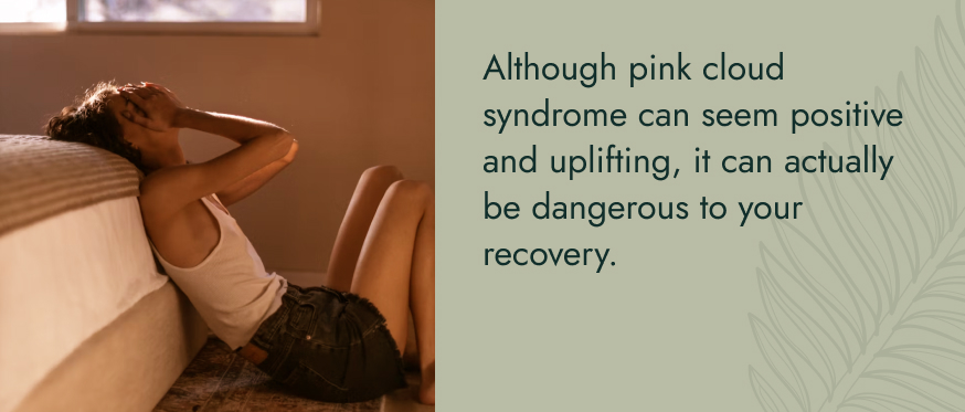 Image: A woman sitting on the floor, leaning against a bed with her head in her hands. Text: Although pink cloud syndrome can seem positive and uplifting, it can actually be dangerous to your recovery.