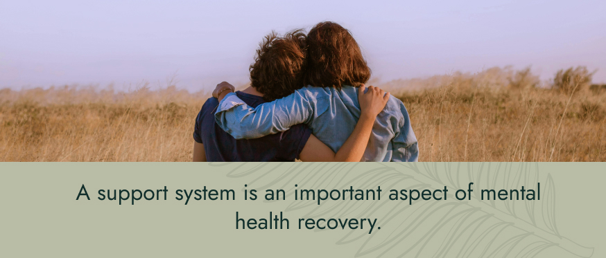 Image: two people look at a landscape with their arms around each other. Text: A support system is an important aspect of mental health recovery.