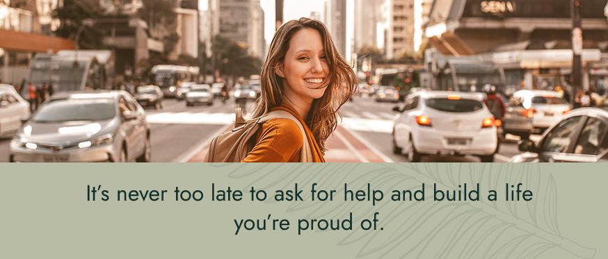 Image: A person walking through a city appearing happy. Text: It’s never too late to ask for help and build a life you’re proud of.