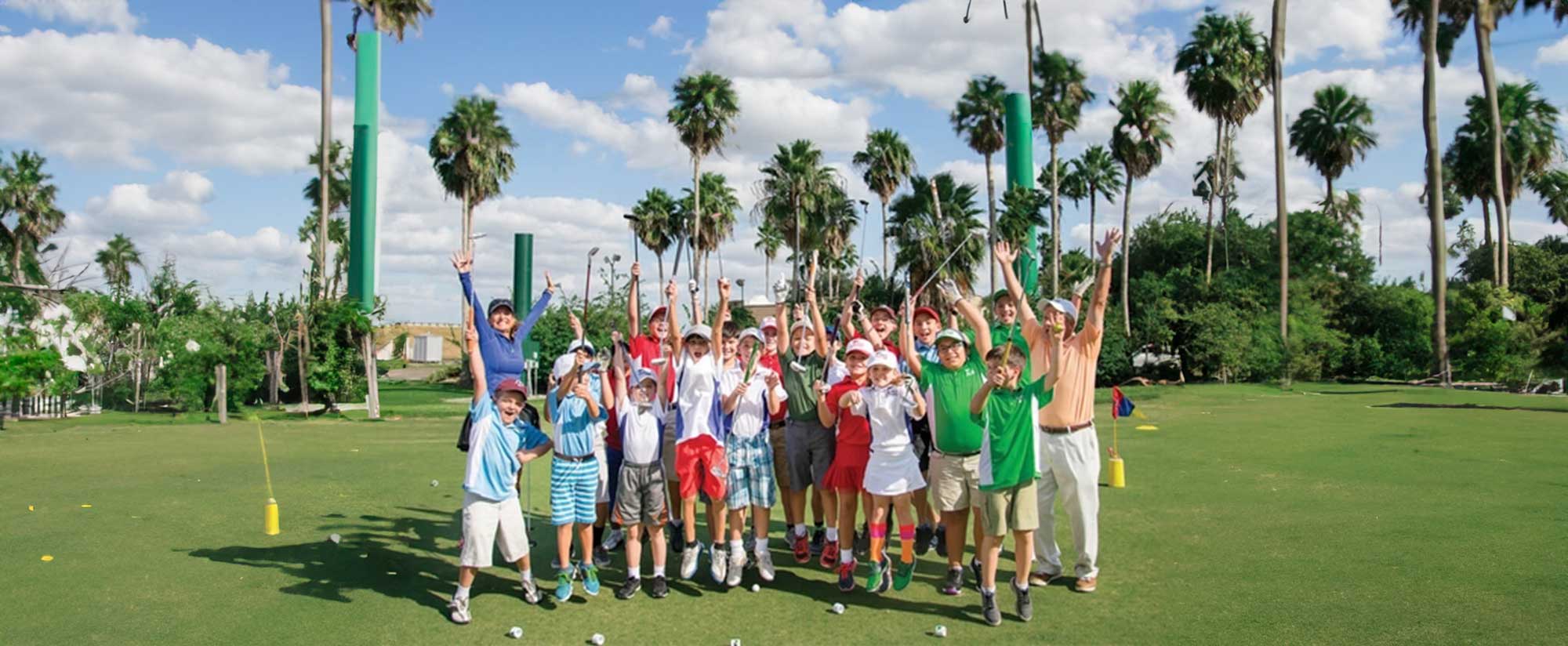 Group of children and an adult celebrating with golf clubs raised on a sunny golf course surrounded by palm trees.