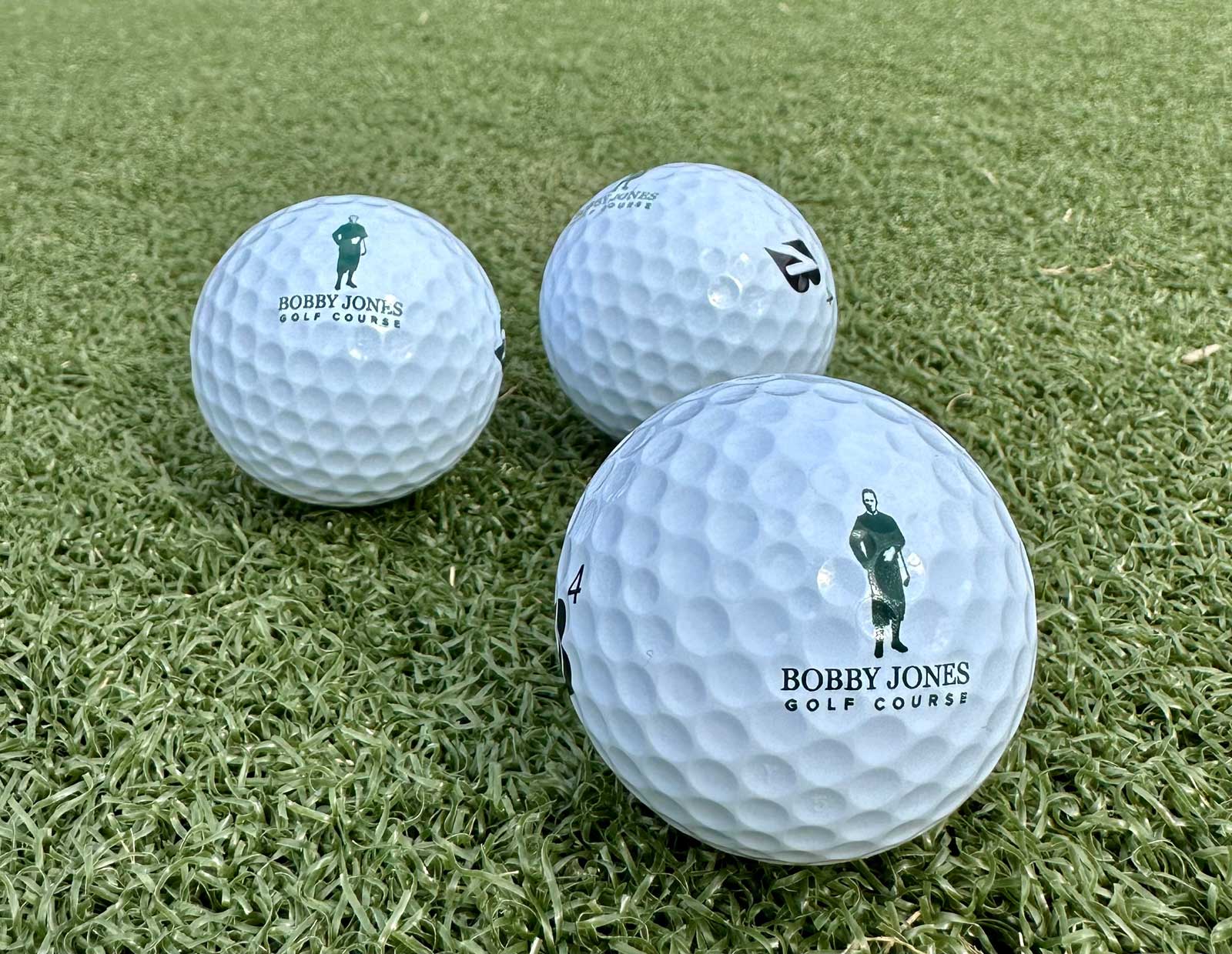 Three golf balls on green grass with Bobby Jones Golf Course logo printed in green.