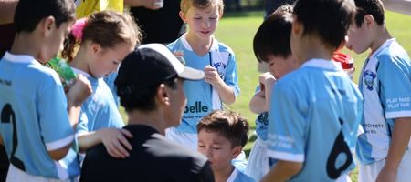 Young soccer players in light blue jerseys on a grassy field, two of them shaking hands.