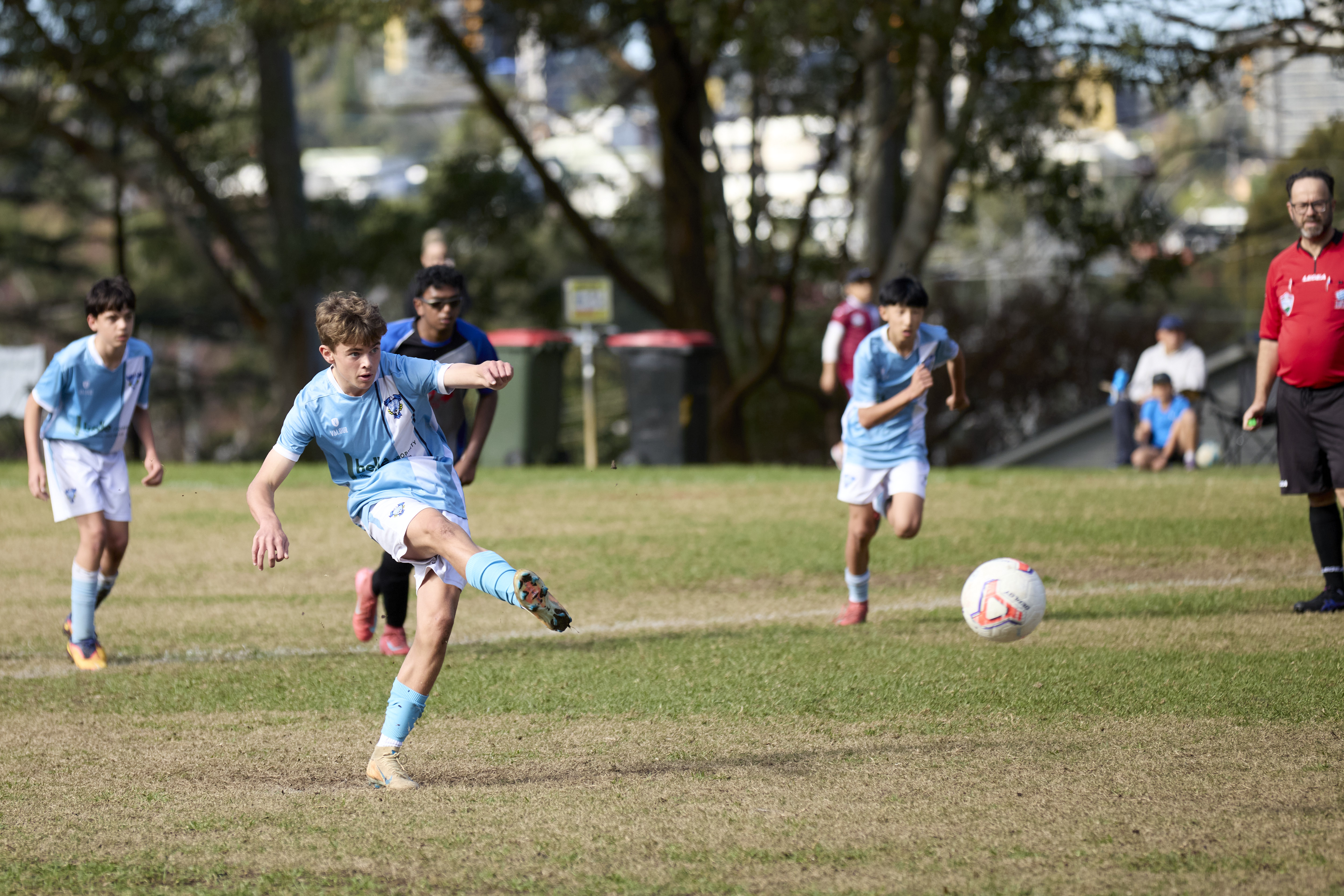 Young soccer players in light blue jerseys on a grassy field, two of them shaking hands.