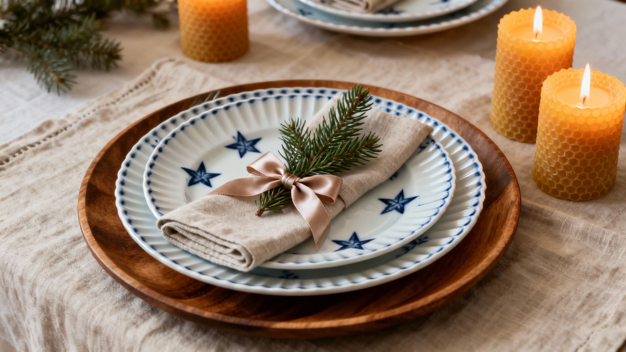 A beautiful Christmas table setting with star-fluted plates, linen napkin, spruce sprig, and beeswax candles.