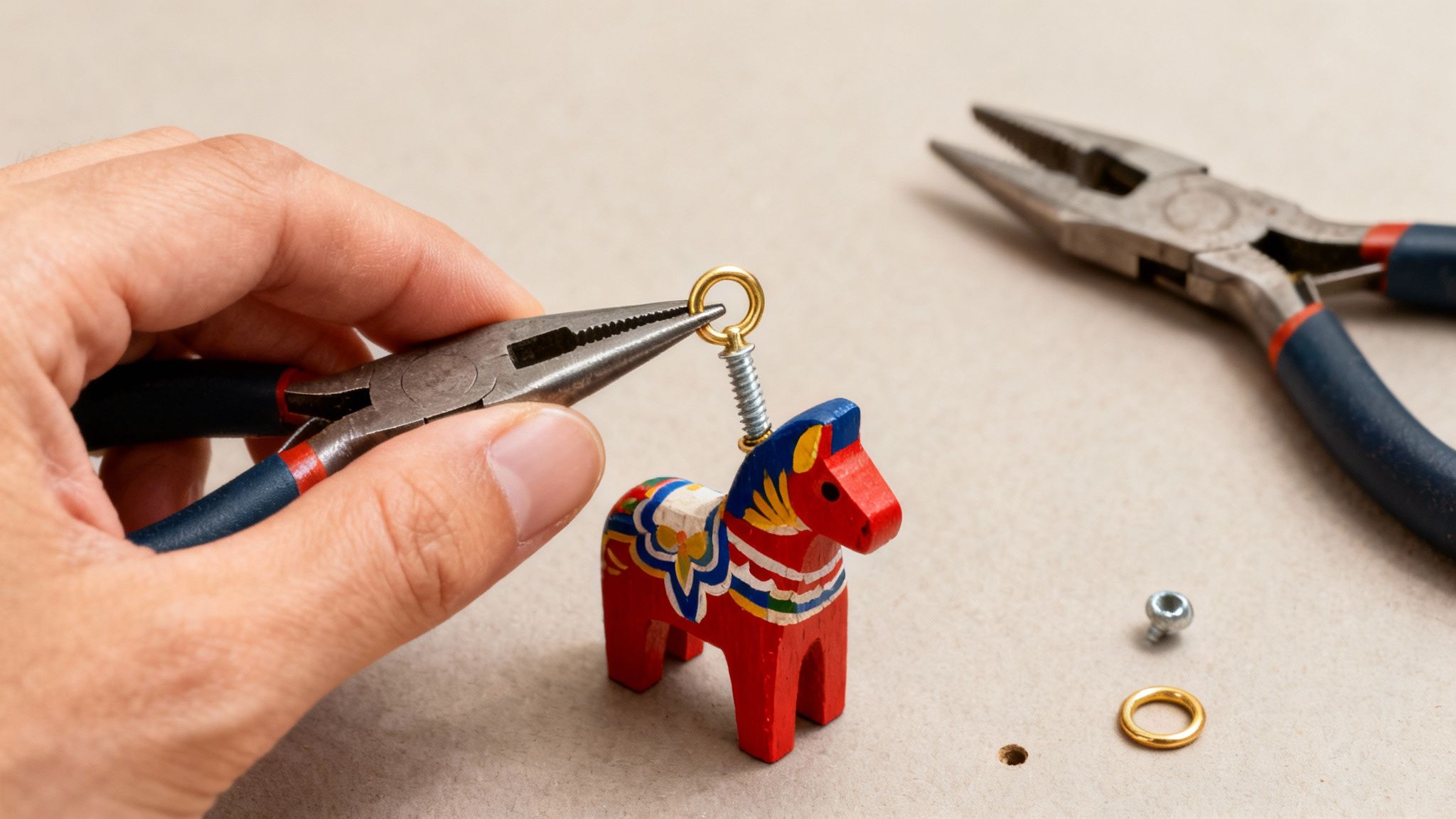 A hand uses pliers to attach a golden ring to a spring on a red wooden horse.