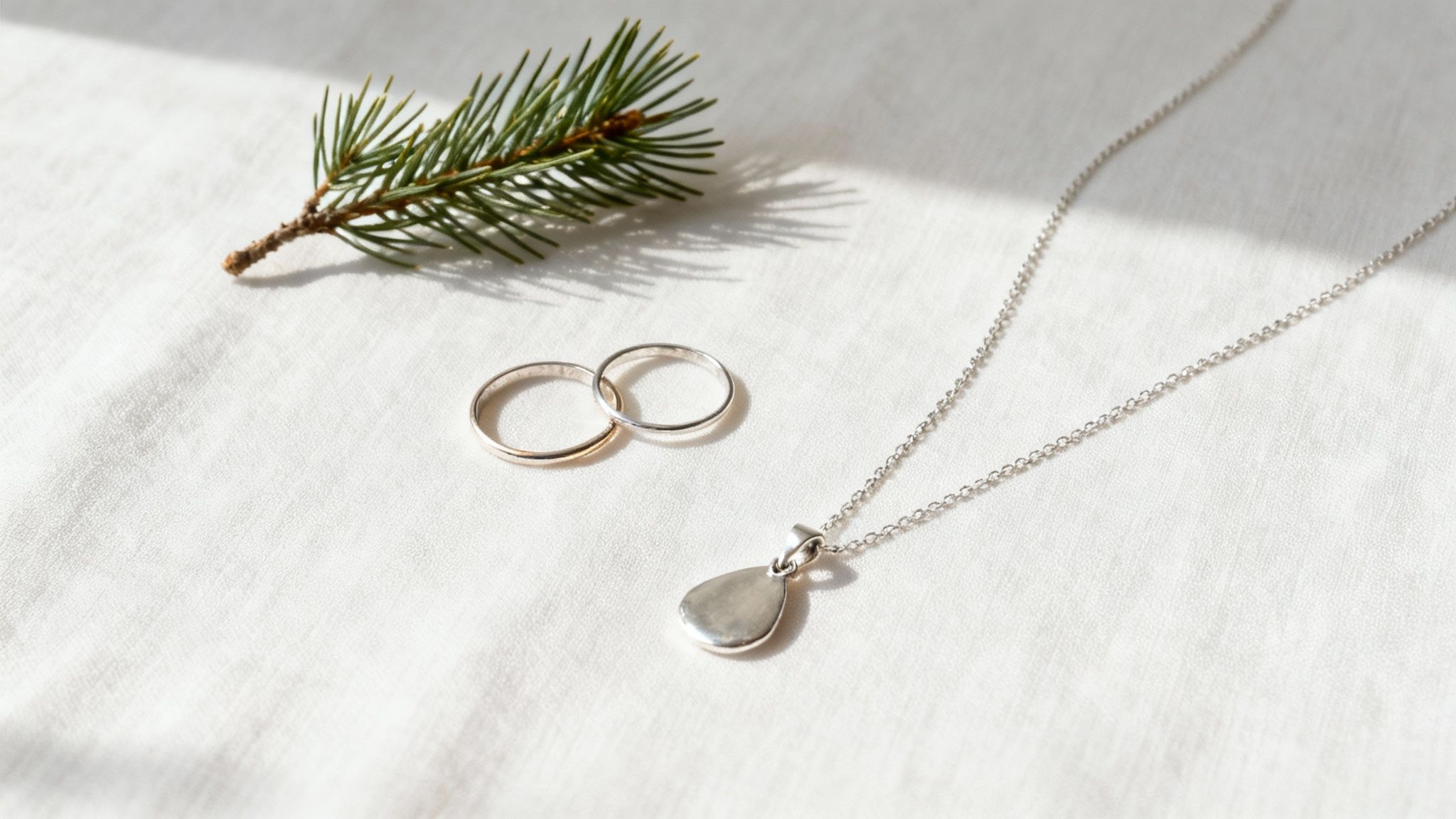 Elegant silver and gold jewelry, including a necklace and rings, with a pine branch on white fabric.
