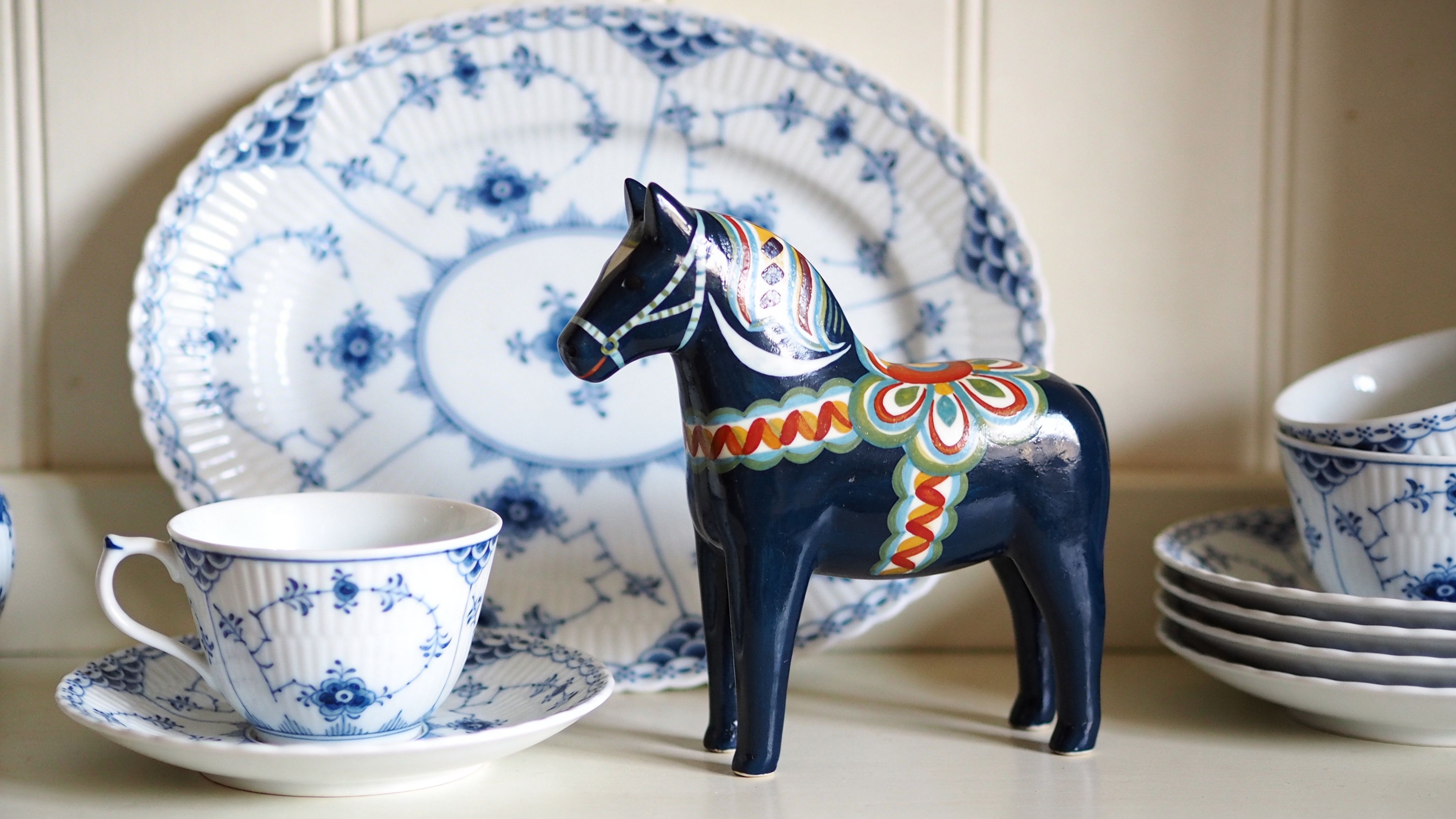 A classic blue Royal Copenhagen porcelain teacup set sitting beside a decorative traditional dark blue Dala horse.