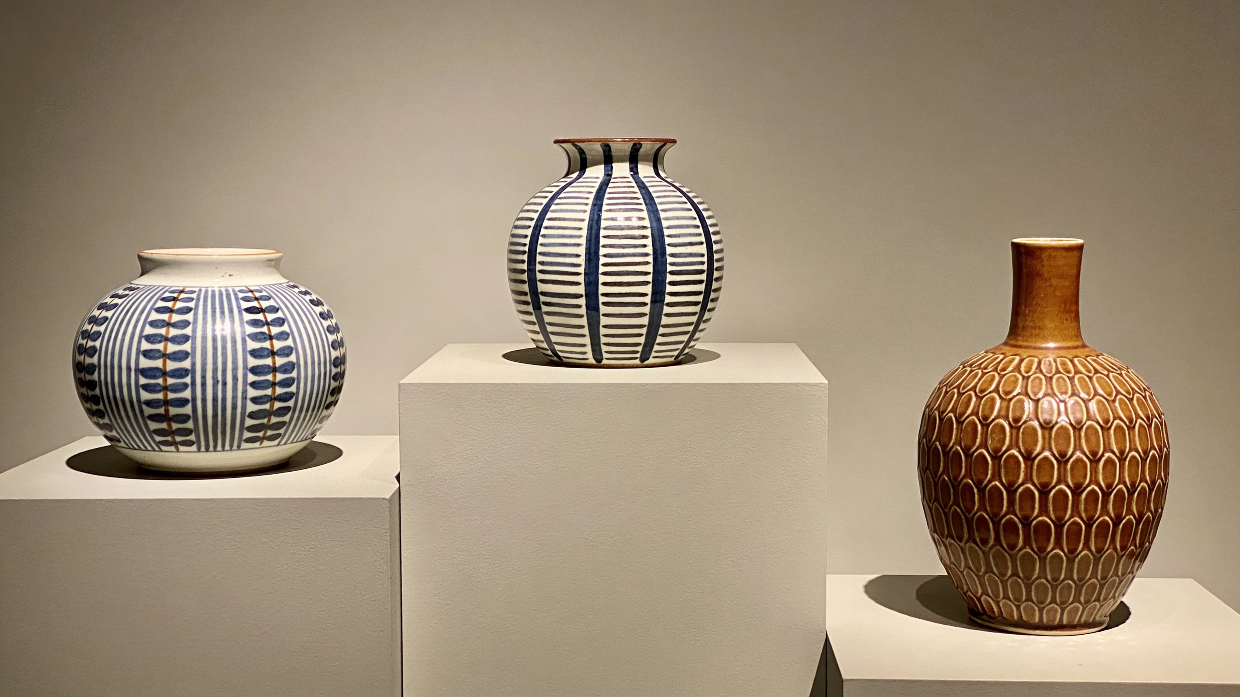 Three decorative ceramic vases with unique blue-and-white patterns and a brown textured finish displayed on pedestals.