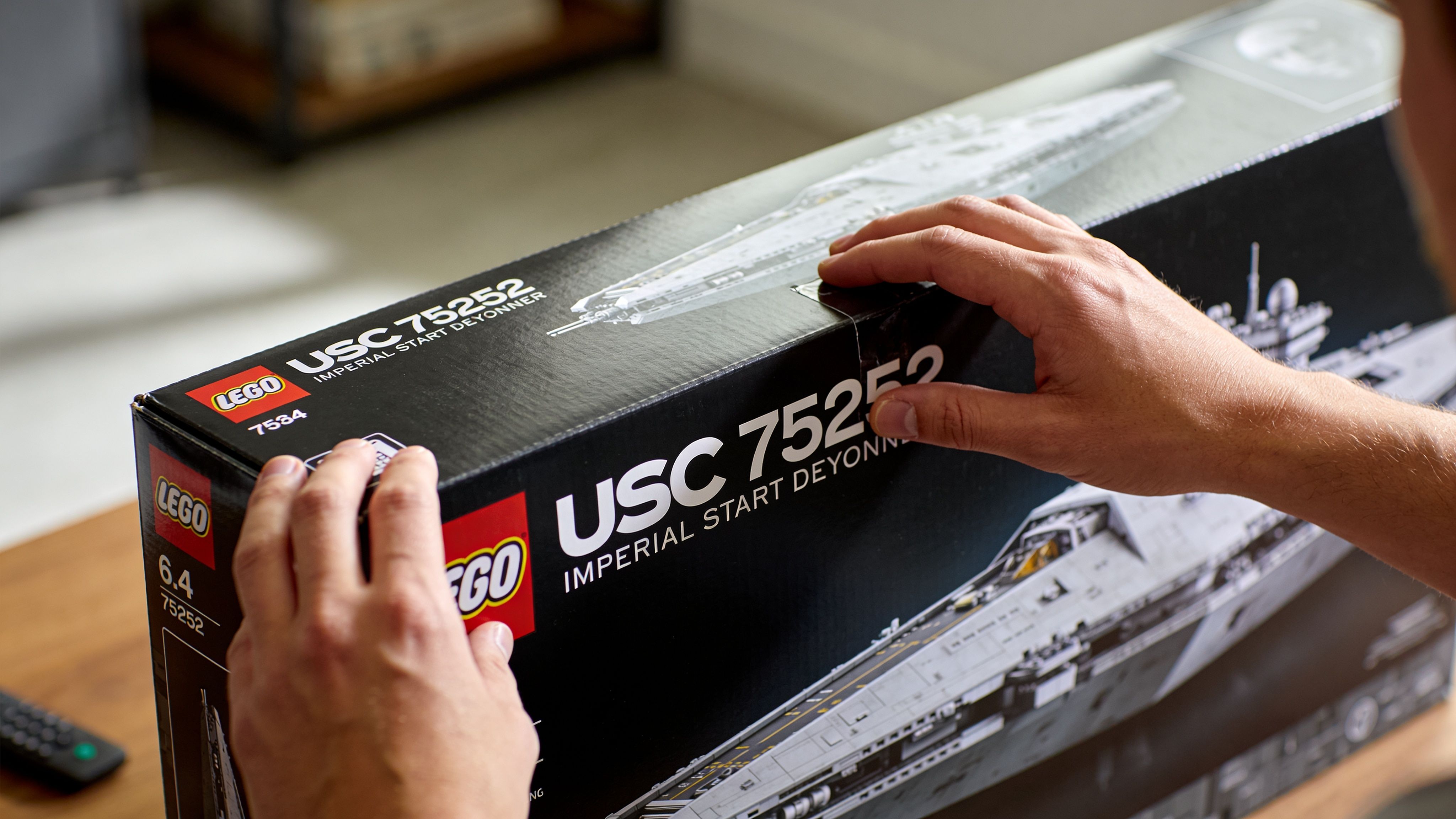 A person holding a large LEGO Star Wars Imperial Star Destroyer building set box on a table.