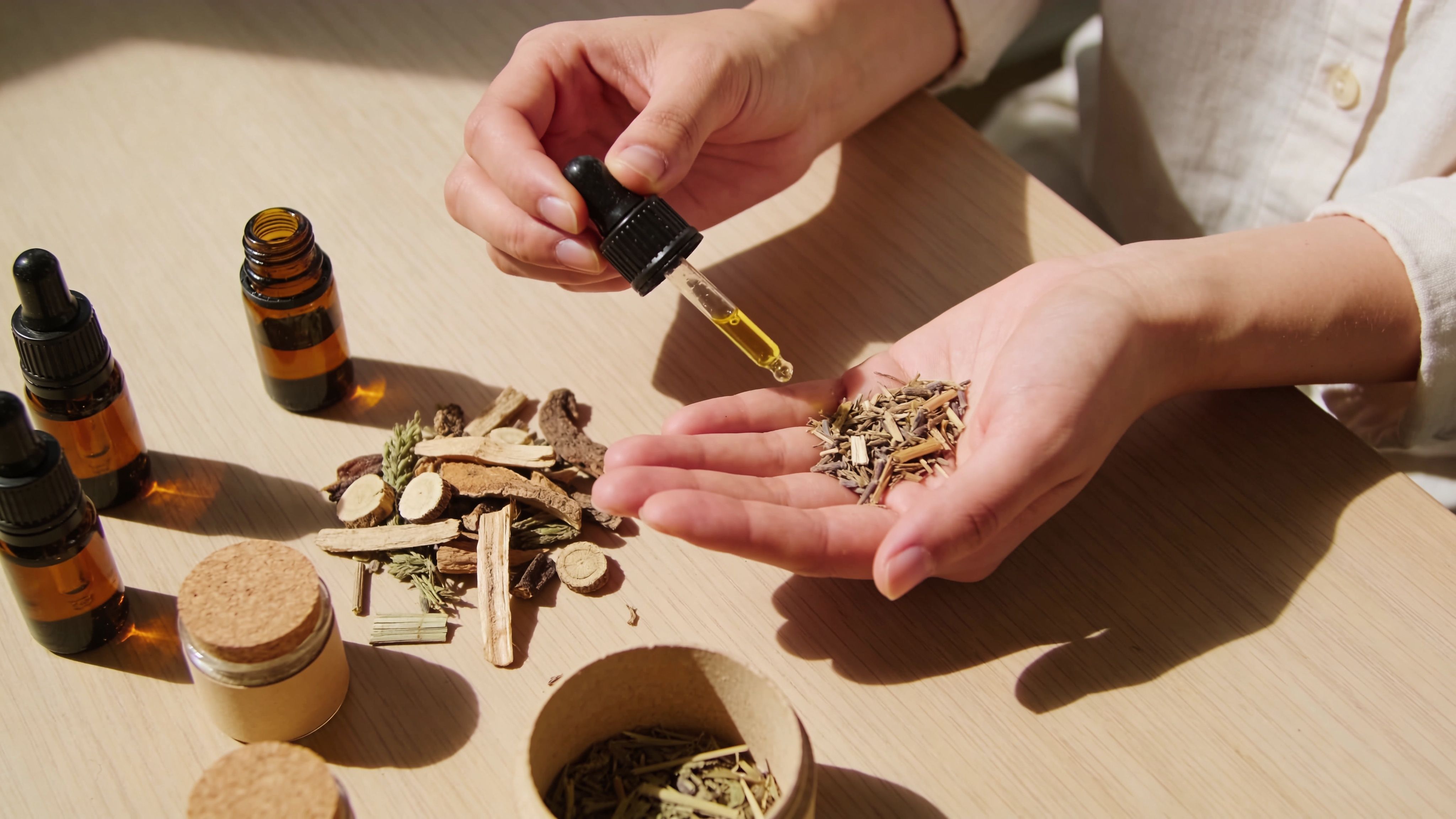 A person uses a dropper to place essential oil onto dried herbs held in their open palm.