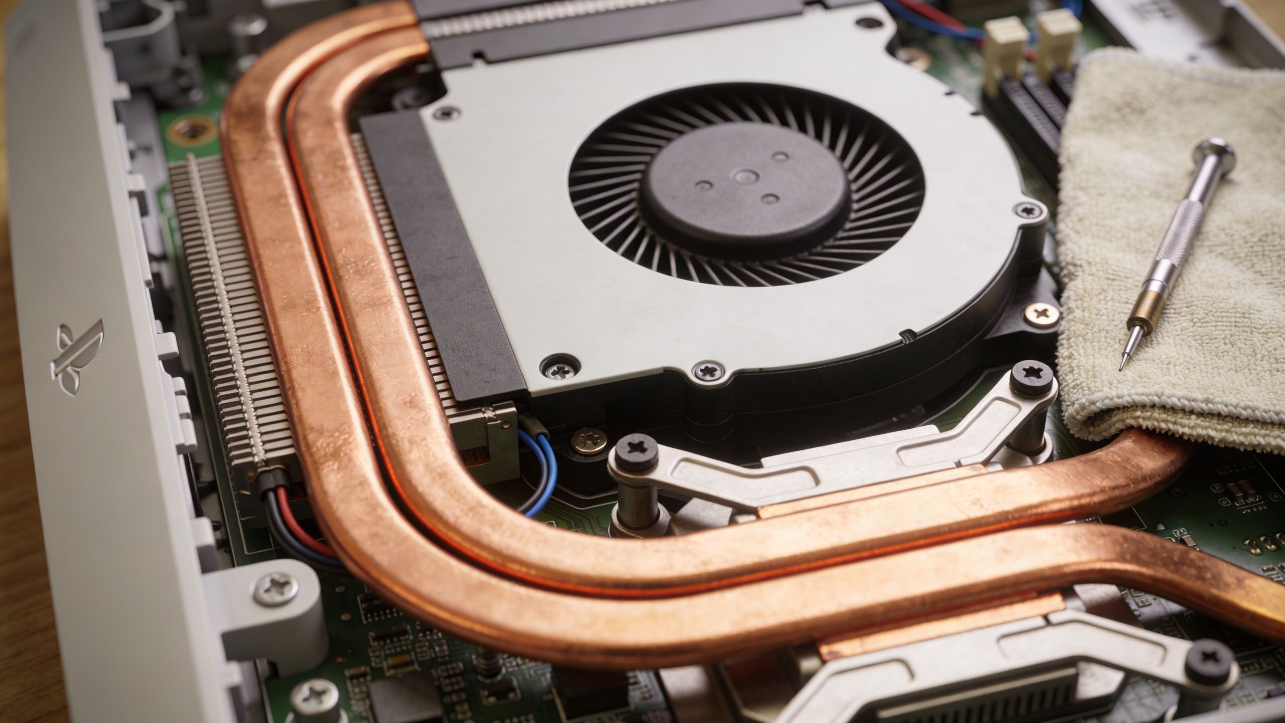 Internal components of a disassembled PlayStation 3 console showing the cooling fan, heat pipes, and repair tools.