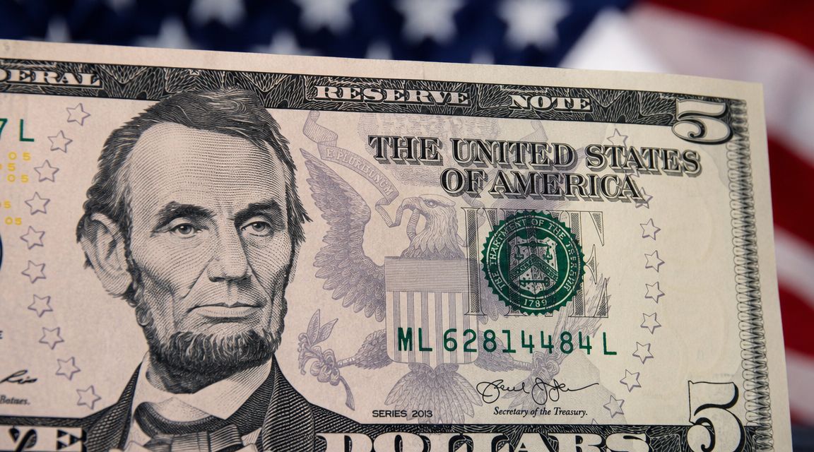 A close-up view of a five dollar bill featuring Abraham Lincoln against an American flag background.