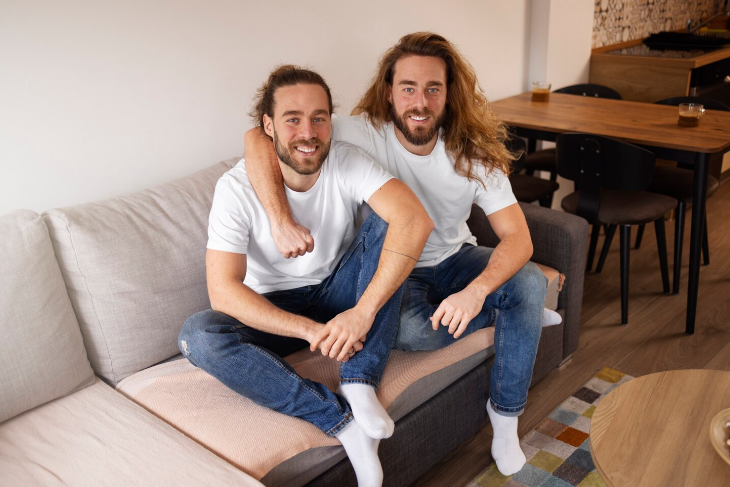 Two men smiling at the camera while sitting on a couch in a recovery home