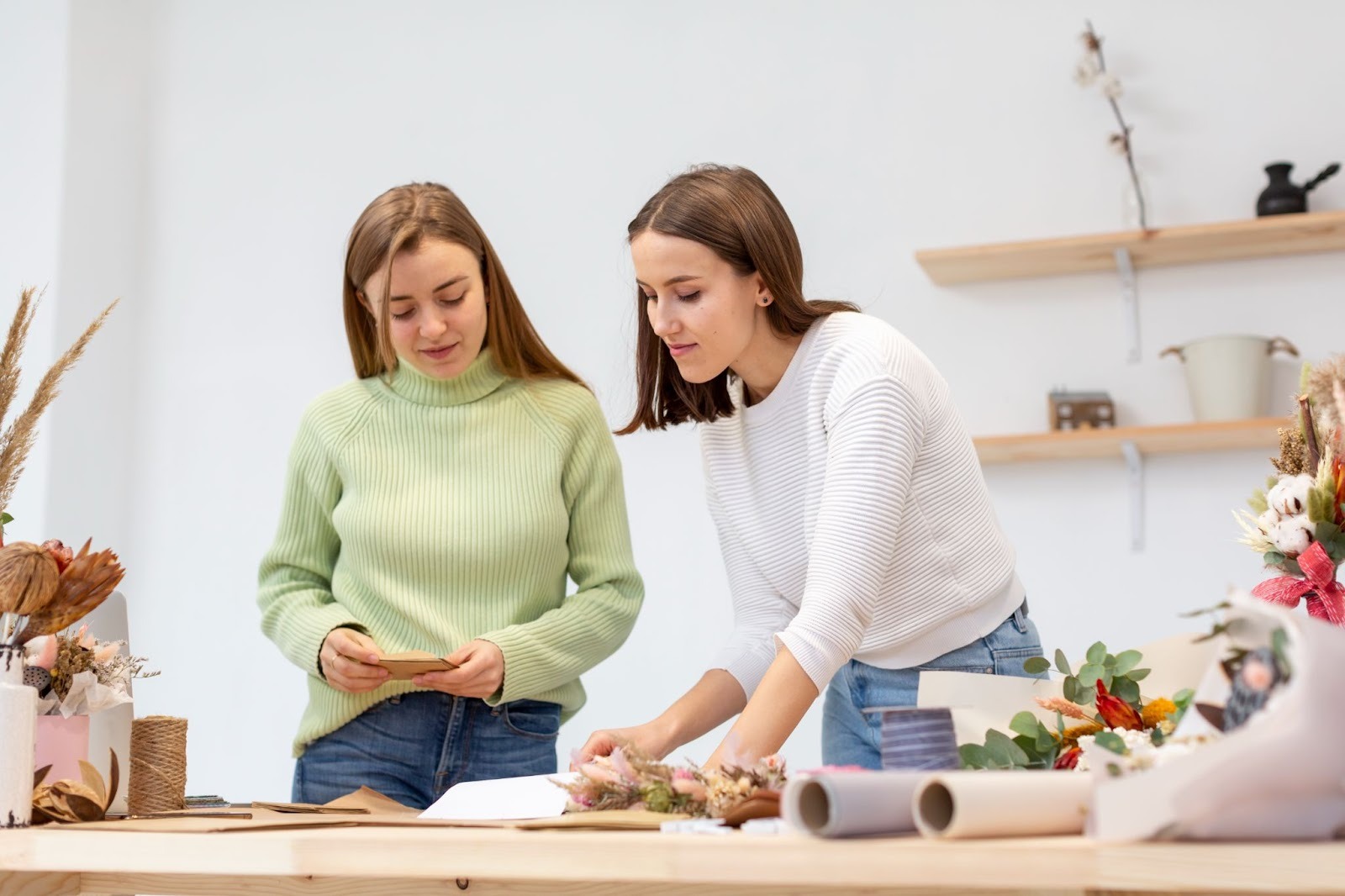 Two women stand beside a table adorned with a colorful arrangement of flowers, demonstrating the skill-building aspect of recovery homes
